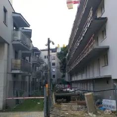 Budowa bloków mieszkalnych, gdzie widać niedokończone balkony i materiały budowlane. Typowa patodeweloperka, która nie budzi zachwytu.