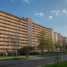 Długi, pomarańczowy falowiec gdańsk ciągnie się wzdłuż ulicy, z balkonami i oknami.