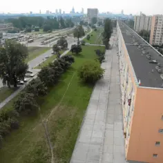 Długi, pomarańczowy blok mieszkalny, prawdopodobnie najdłuższy blok w Polsce, z widokiem na tory tramwajowe i panoramę miasta.