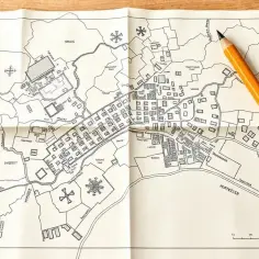 Ołówek leży na złożonej mapie do celów projektowych, przedstawiającej szczegółowy plan miasta z nazwami ulic i budynków.