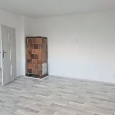 Puste pomieszczenie z piecem kaflowym i drzwiami. To może być przyszłe mieszkanie komunalne po remoncie.