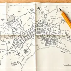 Mapa zasadnicza przedstawia szczegółowy plan miasta Aderigh z zaznaczonymi budynkami, rzekami i polami. Obok leży żółty ołówek.