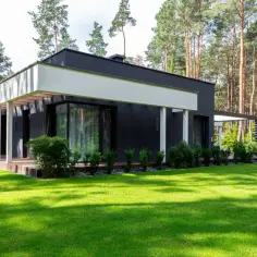 Nowoczesny dom z dużymi oknami i tarasem, otoczony zielonym ogrodem i lasem. Zastanawiasz się, jaki jest koszt budowy domu 150m2?