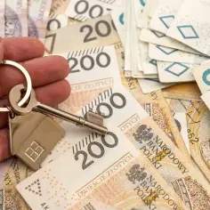 Dłoń trzyma klucz z breloczkiem w kształcie domu na tle polskich banknotów. Zastanawiasz się, zachowek ile?