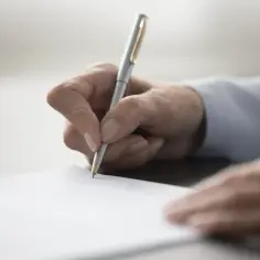 Dłoń pisze długopisem na papierze, przygotowując dokument. Dowiedz się, jak napisać testament.