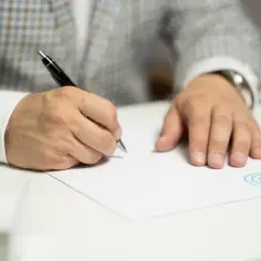 Mężczyzna w eleganckim garniturze składa wniosek o stwierdzenie nabycia spadku, podpisując dokument piórem.