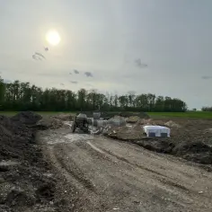 Budowa w toku. Betonowa dylatacja co to? Widać koparkę, materiały budowlane i przygotowany teren pod fundamenty.
