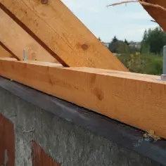 Drewniana belka, czyli murłata, jest przykręcana do betonowego wieńca za pomocą śrub. Widać fragment konstrukcji dachu.