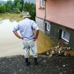 Mężczyzna w kapeluszu patrzy na wodę sięgającą do okien domu. To skutki powodzi błyskawicznej.