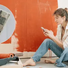 Kobieta planuje remont mieszkania, trzymając w ręku telefon i pieniądze. Dostępna dotacja na remont mieszkania ułatwi prace.
