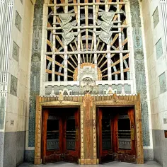 Monumentalne drzwi i okno w stylu art deco, ozdobione geometrycznymi wzorami i stylizowanymi motywami.