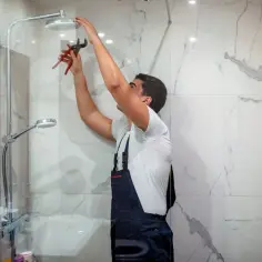 Instalator kończy biały montaż prysznica, dokręcając słuchawkę kluczem.