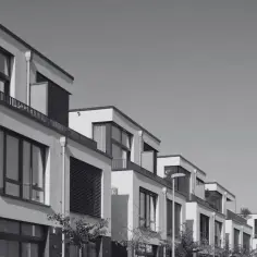 Nowoczesne domy szeregowe z dużymi oknami i balkonami. Widać fragmenty zieleni i ulicę z kierunkowskazem. Suterena jest częścią tej architektury.