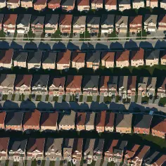 Rzędy identycznych domów z dachami w różnych kolorach, symbolizujące suburbanizację.