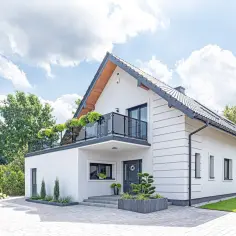 Nowoczesny biały dom z balkonem i zielenią. Idealny przykład darmowych projektów domów, które inspirują do budowy.