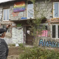 Budynek z graffiti, w tym "Anarchia" i "Stop Policji". Mężczyzna gestykuluje, a w oknie siedzi osoba. To miejsce, gdzie żyją squatersi.