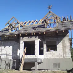 Na dachu budowanego domu, wśród drewnianej konstrukcji, widoczna jest ozdobna **wiecha**.