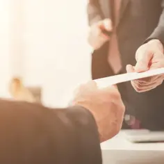 Dwie dłonie w garniturach podają sobie białą kartkę. Czy to umowa najmu? Kim jest najemca?