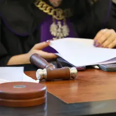 Sędzia w todze z łańcuchem i orłem przegląda dokumenty. Obok młotek sędziowski i telefony. Sprawa dotyczy wydziedziczenia.