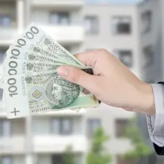 Dłoń w garniturze trzyma banknoty 100 zł. Może to być pomoc w uzyskaniu dodatku mieszkaniowego na nowe lokum.