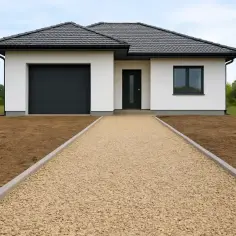Nowy dom z nowoczesnym garażem i wejściem. Podjazd z jasnego kruszywa prowadzi do drzwi.