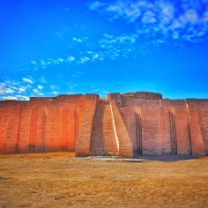Starożytny ziggurat z cegły, monumentalna budowla wznosząca się ku błękitnemu niebu z chmurkami.