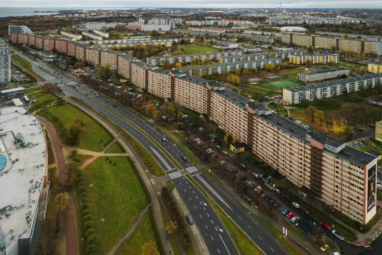 Długi, falisty budynek mieszkalny, znany jako falowiec gdańsk, otoczony zielenią i drogą z samochodami.