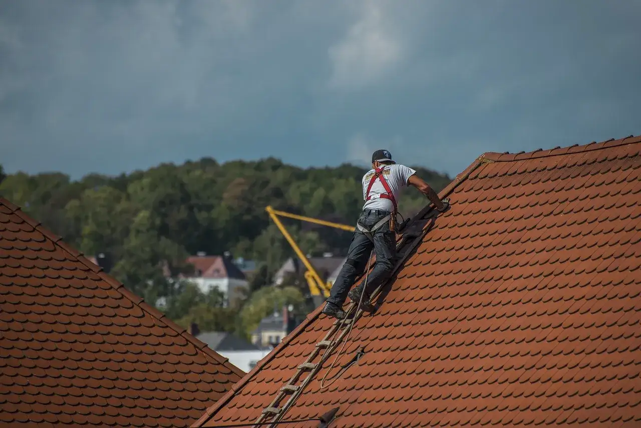 Pracownik w asekuracji wspina się po dachu pokrytym dachówką, która przypomina eternit.