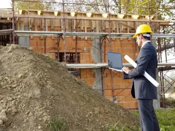 Inżynier w kasku analizuje plany budowy na laptopie, uwzględniając poziom wód podziemnych.